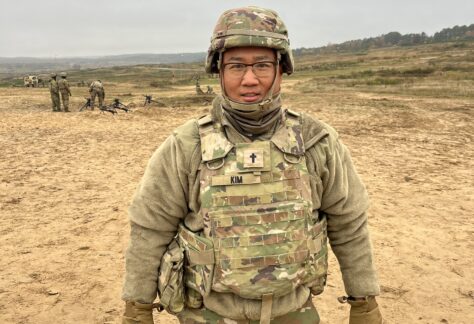 Military chaplain in uniform standing on training field with troops in background